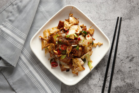 Stir fried pork slices with vegetables with black chopsticks resting on the surface counter