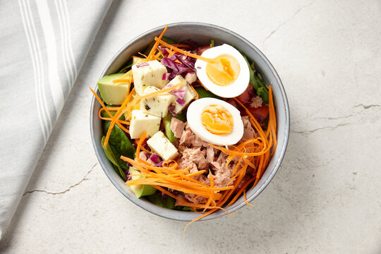 A bowl of tuna salad topped with boiled egg and cubed cheese