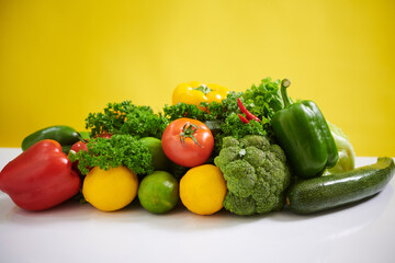 Bright collection of colorful vegetables displayed on white table against vibrant yellow backdrop, showcasing freshness and variety in an appealing composition