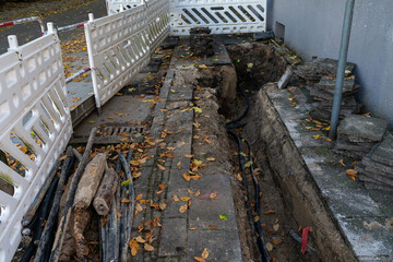 Workers are digging a trench beside a building to install utility lines, surrounded by fallen...