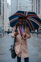Businessman using smart phone walking with umbrella in new york city