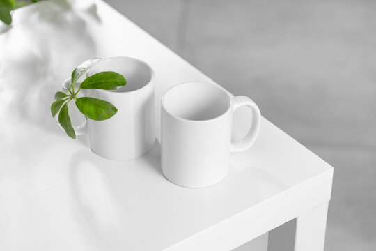 Mockup of a white tea cup or coffee mug on a white table in a Scandinavian style kitchen with a houseplant Scheffler plant. Subject template for your design, advertising with copy space