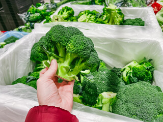 Woman chooses fresh organic broccoli in grocery store. Woman hand take broccoli from shelf of store. Healthy food, shopping concept