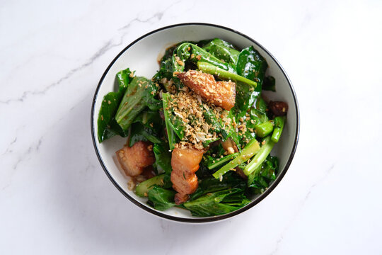 Stir-fried green leafy vegetable with deep fried pork belly garnished with crushed peanuts.