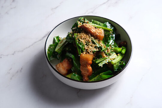 Stir-fried green leafy vegetable with pork belly slices garnished with crushed peanuts.