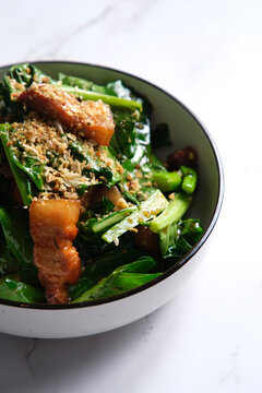Stir-fried green leafy vegetable with pork belly slices garnished with crushed peanuts.