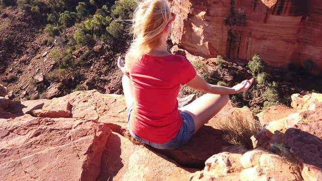 Peaceful woman doing yoga meditation in lotus pose at edge of Kings Canyon in Watarrka National Park with vertical rock walls in front. Outback Red Center, Northern Territory, Australia.