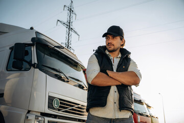 Serious facial expression, arms crossed. Truck driver is near the transport outdoors