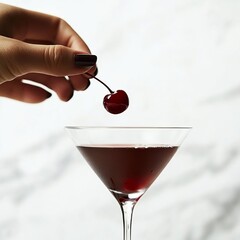 a glass of drink and a hand dipping a cherry into it