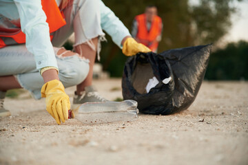 Picking up the bottle. A volunteers collects garbage on a muddy beach
