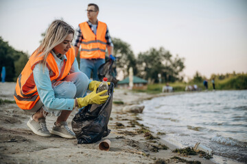 On the shore. A volunteers collects garbage on a muddy beach