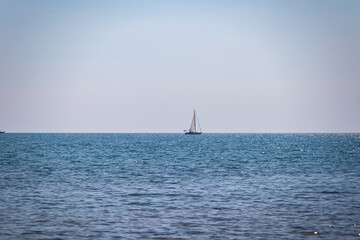 Fototapeta premium Lone sailing boat on horizon of shimmering idyllic Adriatic Mediterranean sea. Serene coastal scene with blue sky and calm turquoise water in Karigador, Istria, Croatia. Luxury summer vacation