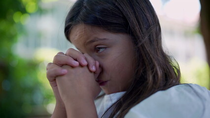 Girl clasping her hands together, eyes closed in deep concentration, evoking a sense of spirituality, hope, and faith. peacefulness in a natural setting
