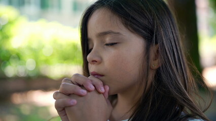 Girl with eyes closed, hands clasped together in a prayer-like position, symbolizing spirituality, hope, and faith. peaceful reflection