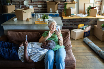 Senior couple relaxing on couch with smartphones after moving in
