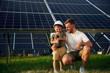 Posing with drill in hands. Father with his little son are together near the solar panels