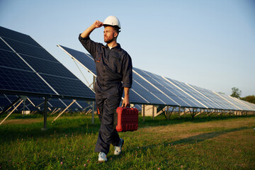 Touching the white hard hat. Man is working with solar panels outdoors at daytime