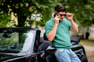 Confident man standing next to his convertible car and having a call