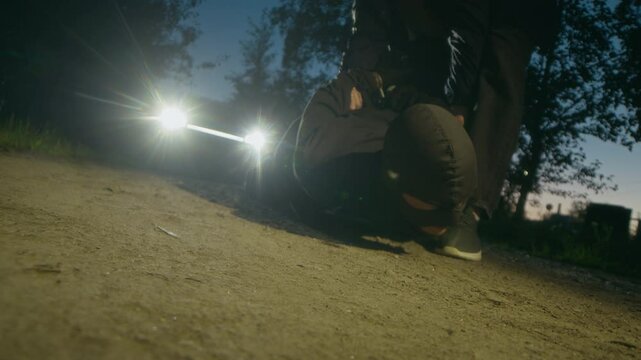 Police officer putting handcuffs on disarmed criminal in black balaclava lying on ground and being pulled towards police car during nighttime arrest