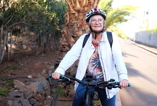 Sporty senior woman with bicycle helmet in healthy outdoor activity with electric bicycle. Happy retired senior lady leads healthy life using bike to mouve