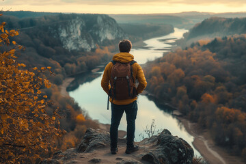 A man stands on a rocky outcrop overlooking a river valley during sunset in the autumn months surrounded by colorful foliage