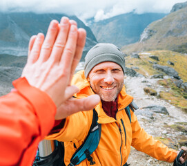 Smiling backpacker dressed orange jacket giving High Five to female mate during Himalaya valley...