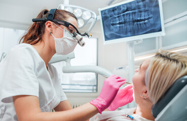 Dentist female doctor dressed uniform in magnifying glasses performing preventive dental care....