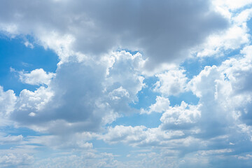 Fluffy white cumulus clouds drift across a bright blue summer sky