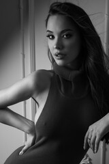 In this captivating black and white photograph, a long-haired brunette model flaunts her figure in a chic, fitted design. The studio's clean lines and subdued tones