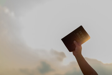 Arm raised into the air with a hand reaching up holding the Holy Bible book and cross on the air....