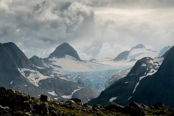 Obraz premium Dramatic sunset over the Swiss Alps with clouds casting soft, muted tones on rugged peaks