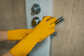 A woman's gloved hands hold a sponge while she cleans a shower area, illustrating attention to detail and commitment to maintaining a spotless environment.