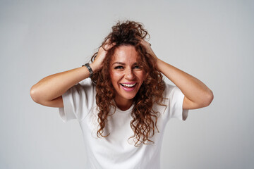 Fototapeta premium A woman in a white shirt and ripped jeans posing positively with a playful expression in a light studio setting
