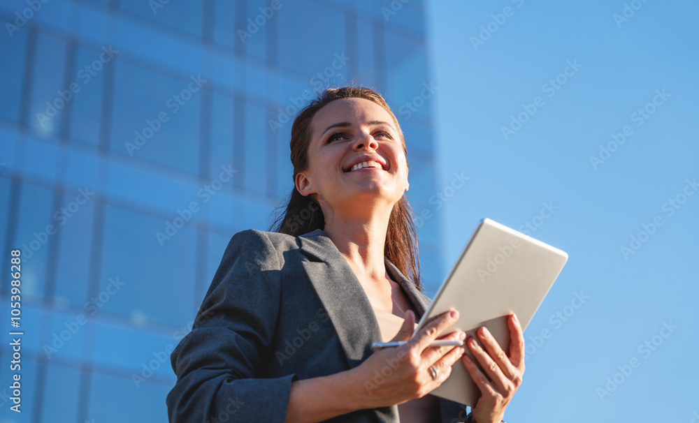 Wall mural Caucasian ethnicity Businesswoman in business casual attire using a digital tablet outdoors in downtown.