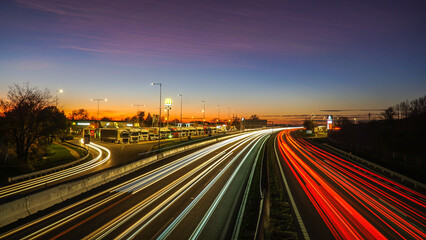 A highway at night, captured in long exposure, glows with vibrant streaks of red and white lights from passing cars, cutting through the dark landscape