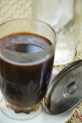 A glass of strong black coffee (Coffea arabica) with grounds, served on a saucer due to heat. Enjoy hot or with ice once cooled. A beloved drink among Indonesians.