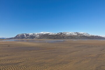 Landscape view of sandy beach and Lavvonjarvarri mountain in the background in clear summer weather, Varanger Peninsula, Norway.