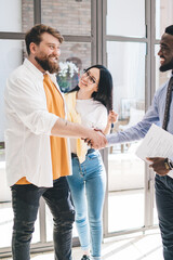 Bearded black realtor with contract and happy couple sealing deal by shaking hands