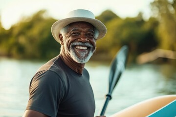 joyful smiling elderly man paddleboarding on serene lake during sunny day. summer leisure at nature, outdoor adventure. senior activity, retirement hobbies, active aging and healthy lifestyle.