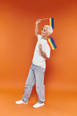 A mature woman with short hair joyfully waves rainbow flags in celebration.