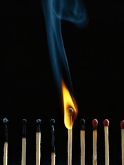 Burning matchstick setting fire to others in a chain reaction on black background