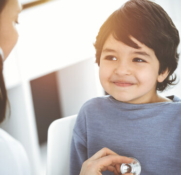 Doctor-woman examining a child patient by stethoscope in sunny clinik. Medicine concept