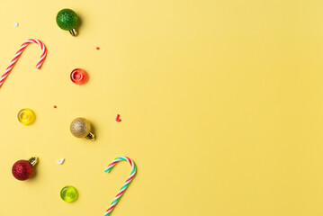 Christmas composition with candy and balls on yellow background from above. Flat lay, top view. Copy space