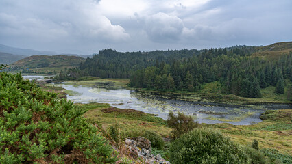 Obraz premium Blick auf das Landschaftsidyll Loch a' Chàirn Bhàin, grüne Gehölze im Vordergrund, dramatische Wolkenstimmung