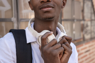 Young african student holding white headphones around neck smiling