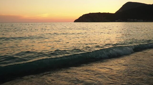 Waves gently lap at shore during stunning sunset over ocean. Golden sunlight reflects off waves as they roll onto shore, creating tranquil atmosphere at sunset by sea. Montenegro summer, Canj