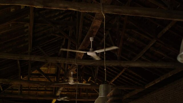 Several ceiling fans slowly rotate on a wooden beamed ceiling with dim lighting in slow motion.