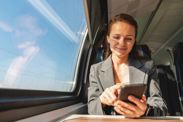 Business travel and commuting. Woman in business attire traveling by modern train and using her...