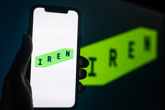 Silhouette of Hand Holding iPhone with IREN Logo in Front of Computer Screen Displaying Logo &ndash; Energy and Utilities Provider  (IREN)