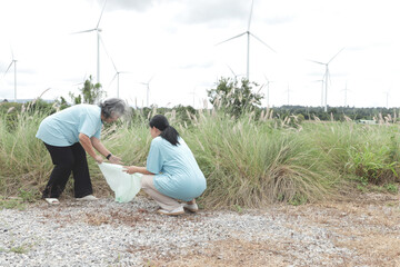Two elderly Asian woman volunteers collecting trash at wind turbine farm. Volunteer cleans up the...